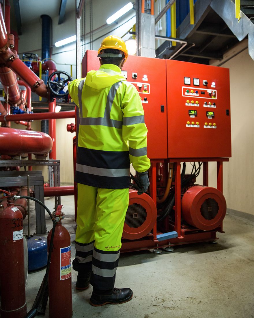 An engineer in hi-vis and a hard hat checking plant-room equipment